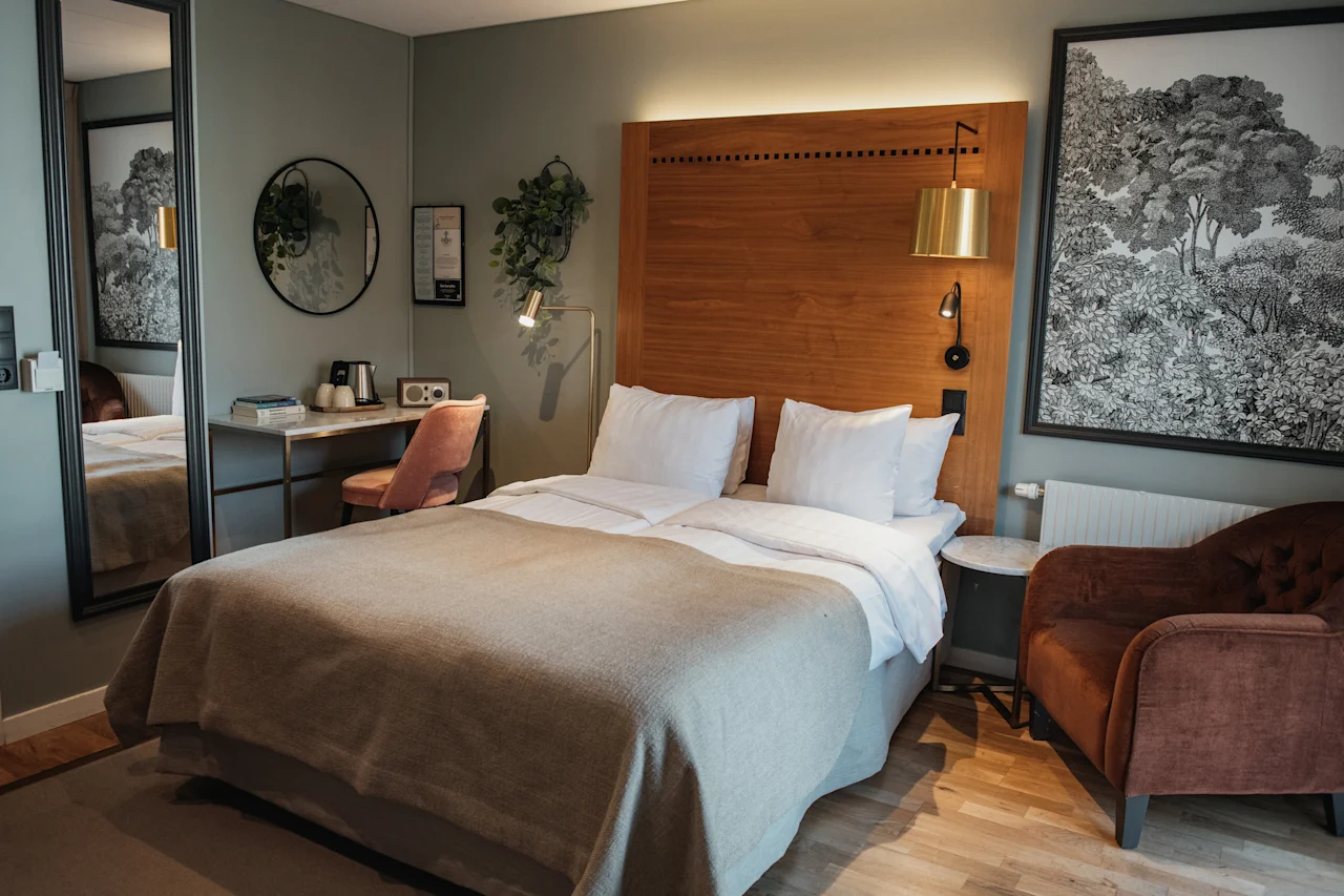 Et koselig hotellrom med en komfortabel seng, et lite skrivebord og en lenestol, designet for avslapning og arbeid.