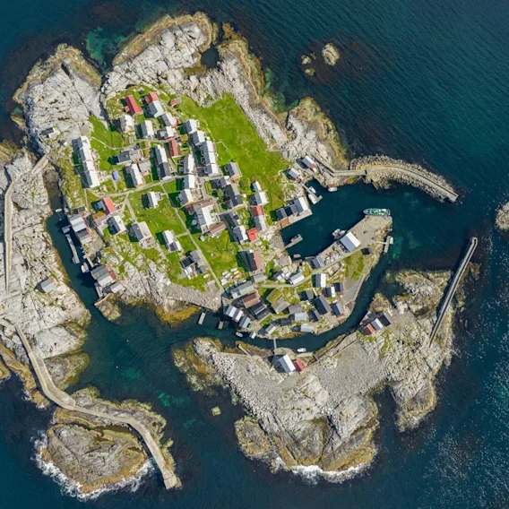 Luftfoto av en liten, steinete øy med tett bebyggelse og en lun havn omkranset av blått hav.