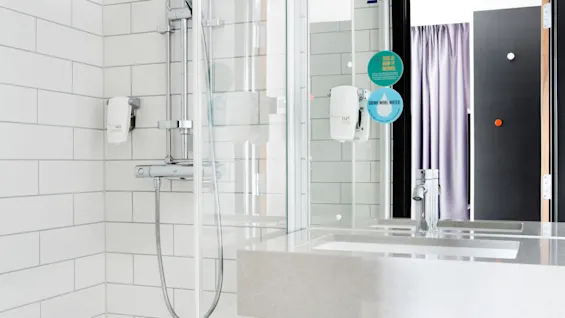 Et moderne badeværelse med en stilfull dusj med hvite fliser og servant reflektert i et speil. Fremtredende tekst inkluderer: "THIS IS HOW IT WORKS: DRINK MORE WATER."