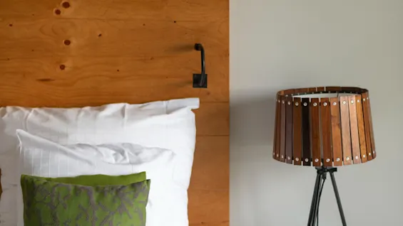 Et hyggeligt soveværelse med en seng, hvide lagner, en grøn pyntepude, en sengegavl i træ og en stilfuld sengelampe.