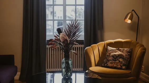 Mysig hotellrumsinredning på Home Hotel Grand, Helsingborg, med en bekväm fåtölj, ett soffbord med blomsterarrangemang och ett fönster.