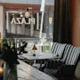 En mysig lounge med randiga fåtöljer vid ett fönster med texten "PLAZA." Ett bord har en liten lampa och växt, omgivna av dämpad belysning och dekorativa element som en glödlampa och vaser.