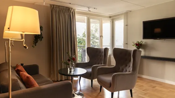 Ett bekvämt och inbjudande vardagsrum med mjuka sittplatser, ett soffbord och ett ljust fönster med utsikt över grönska.