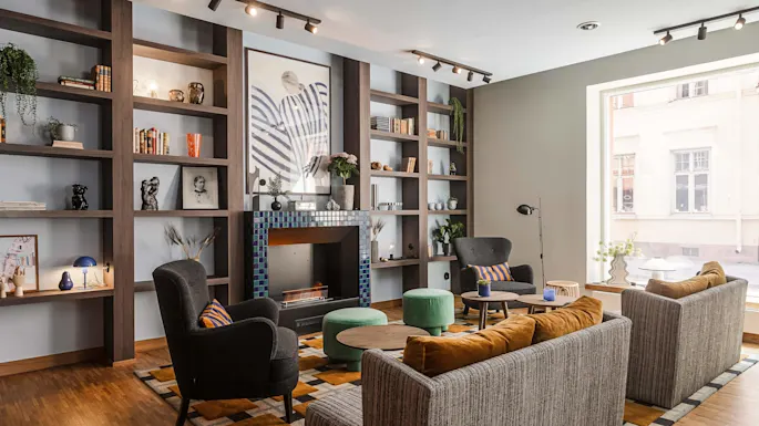 En koselig stue med bokhyller, peis med fliser og et utvalg av moderne møbler, med dagslys som kommer inn gjennom et stort vindu.