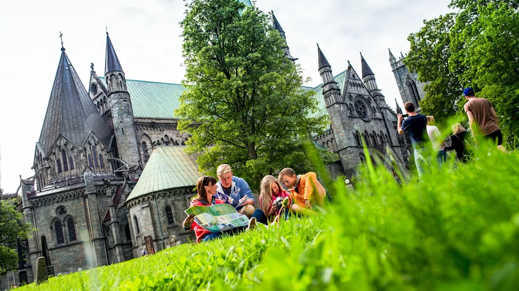 Folk udforsker historiske katedralområder, nogle kigger på et kort, andre nyder landskabet.