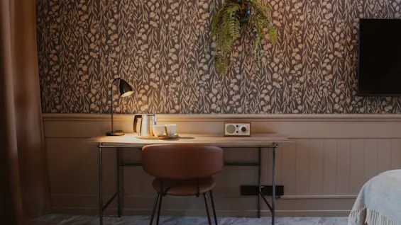 Lämmin ja kutsuva huone, jossa on työpöytä, lamppu, teesetti ja kello, asetettuna koristeellista seinää vasten.