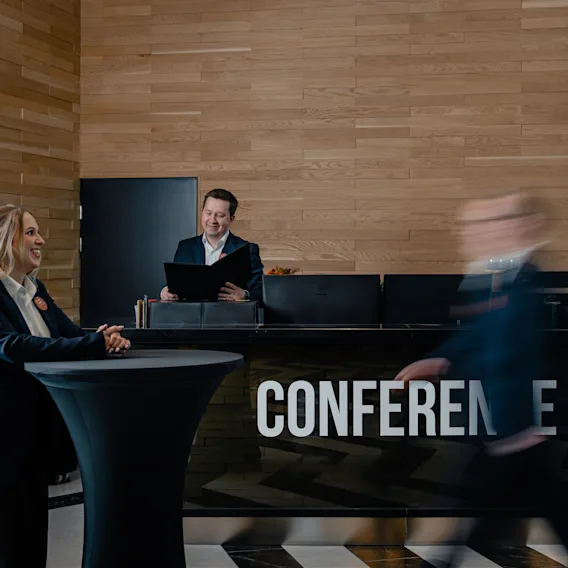 Ihmiset ovat vuorovaikutuksessa konferenssivastaanotossa ystävällisessä ilmapiirissä. Sana CONFERENCE näkyy tiskillä.