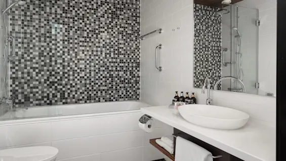 Modern bathroom with mosaic tiled shower, white bathtub, sleek basin, and toiletries.