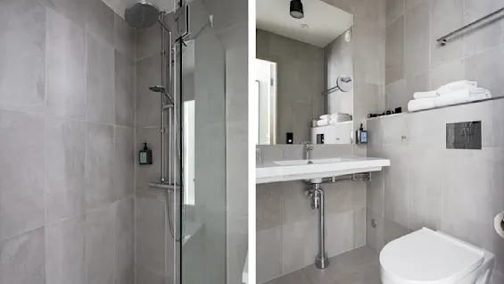Et moderne, lyst bad med grå fliser. Til venstre er en stilren dusj; til høyre et vask med speil og en toalett under sammenbrettede håndklær. En ren og minimalistisk design.