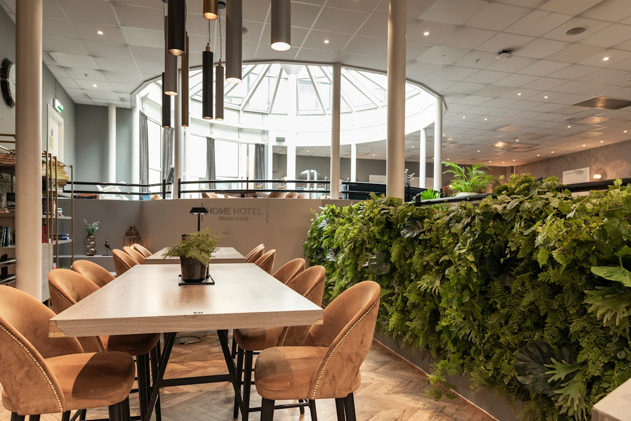 An inviting dining area at Home Hotel Grand Bodø featuring modern tables, comfortable seating, a lush green wall, and a bright skylight.