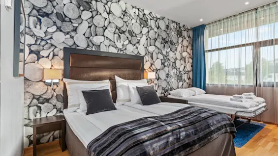 Et koselig hotellrom med en stor seng, en vegg med steinmønster og et vindu med blå gardiner, som tilbyr et komfortabelt opphold.