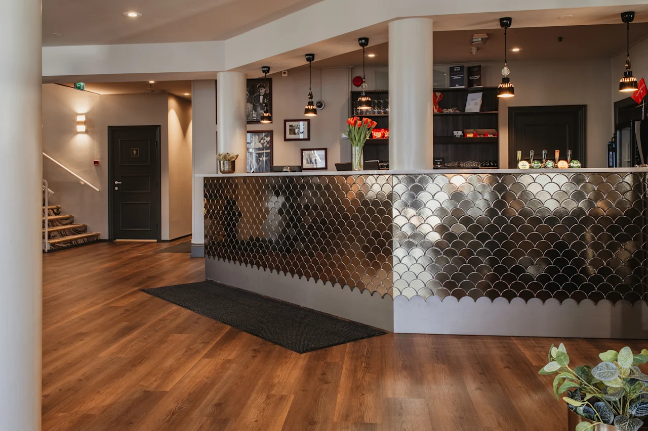 Et moderne hotelreceptionsområde med en stilfuld, metalflisebelagt disk, trægulve og en trappe.