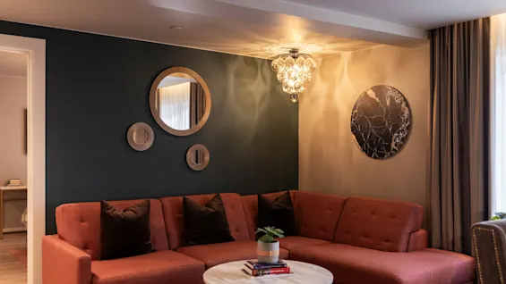 A cozy living room at Home Hotel Grand Bodø with an L-shaped sofa, a round coffee table, and decorative wall art.
