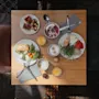 Frukosträtter ligger på ett träbord och visar bakverk, frukt och sallader med apelsinjuice och kaffe. En rosa stol och ett mörkt mönstrat golv omger upplevelsen.