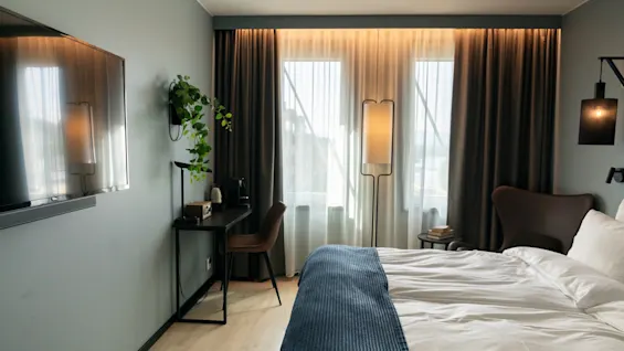 Et moderne hotellrom med en komfortabel seng, et skrivebord og et stort vindu, som skaper et koselig og funksjonelt rom.