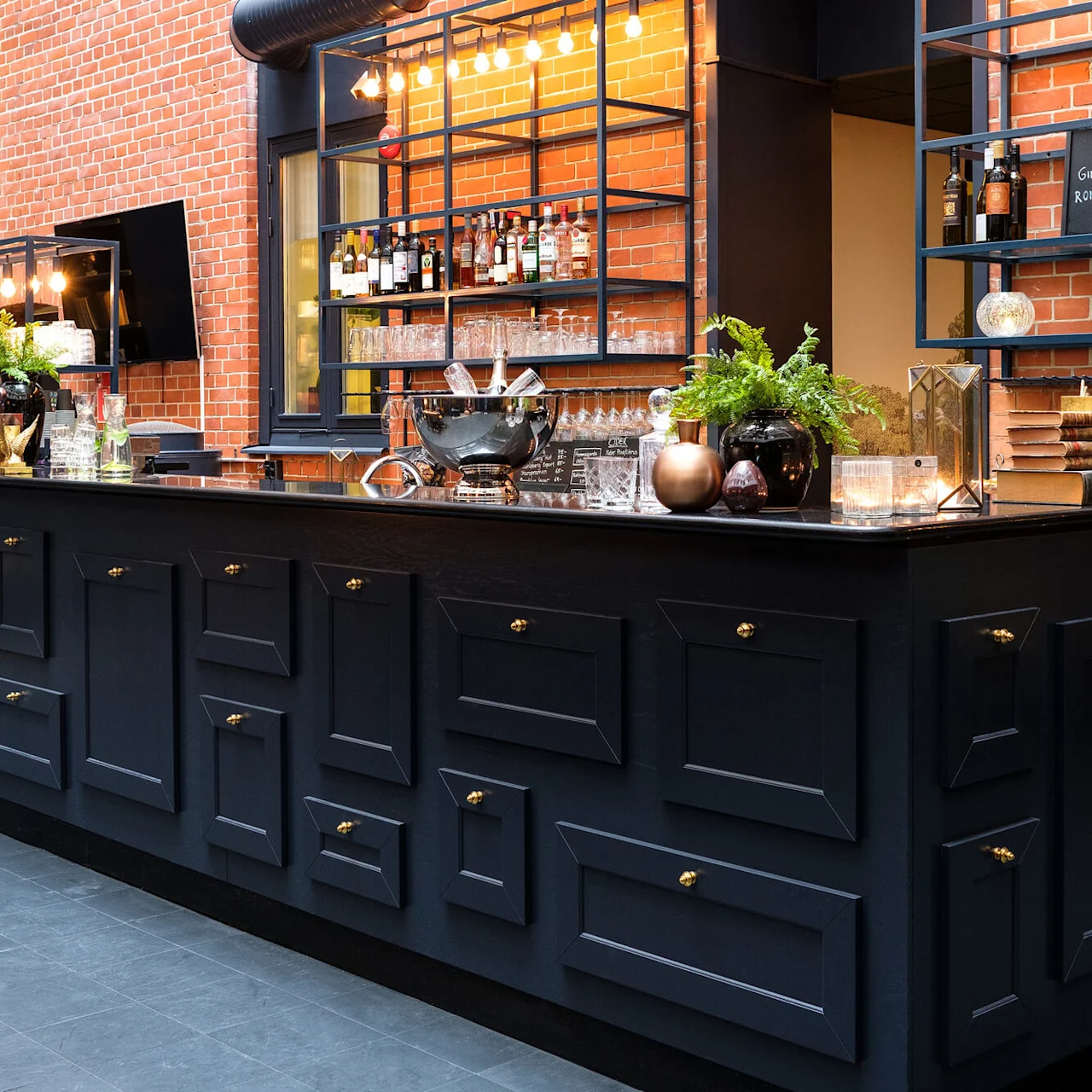 A stylish bar counter with shelves against a brick wall, lit by pendant lights, in an upscale interior.