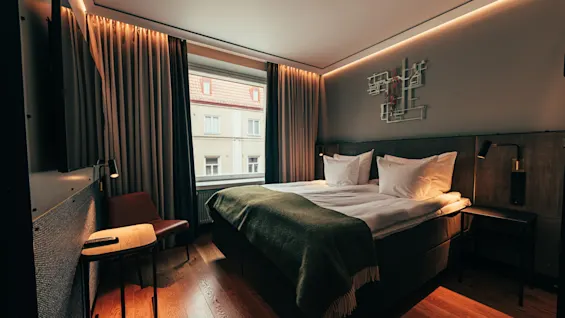 A cozy hotel room with a large bed, warm lighting, and a view of a building outside the window.