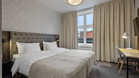 Ett bekvämt hotellrum designat för avkoppling och produktivitet, med en stor säng, ett skrivbord och ett ljust fönster.