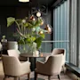 Et stilig restaurantinteriør med et rundt bord, komfortable stoler og en stor plante, satt mot en bakgrunn av mørke vegger og et vindu.
