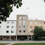 A large building with a sign reading SLOTTSSPARKEN, featuring different facades and flags, framed by green trees.