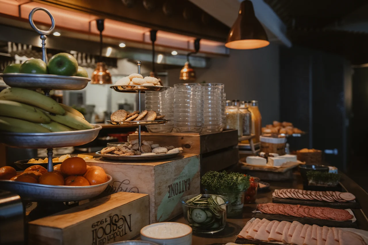 A vibrant buffet spread at Home Hotel Uppsala featuring fresh fruits, a variety of cookies, juices, cheeses, and sliced meats.