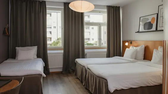 Mukava hotellihuone Home Hotel Uppsalassa, jossa on kolme sänkyä, suuret ikkunat ja modernia seinätaidetta.