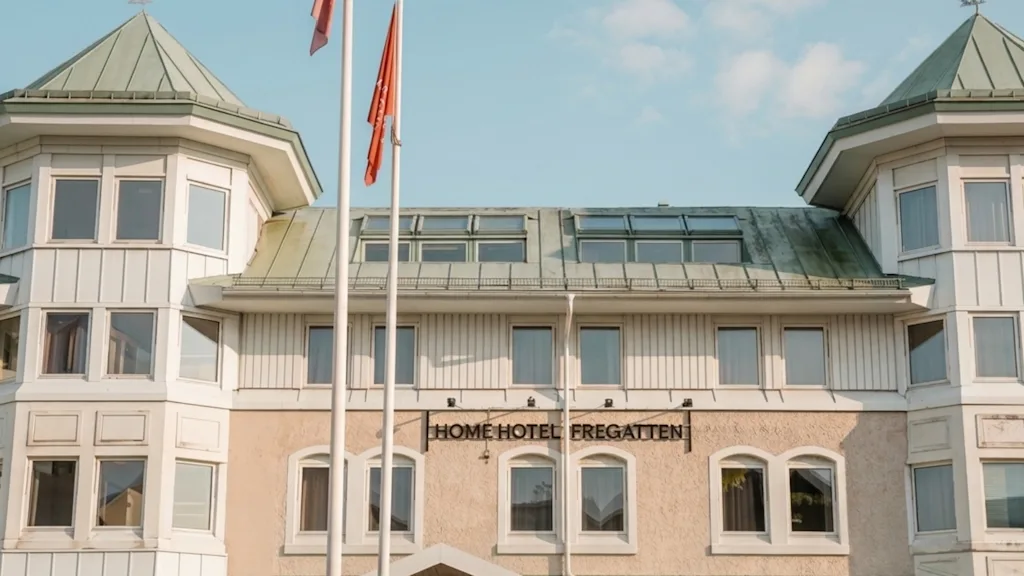 Byggnadens exteriör med en skylt som lyder HOME HOTEL och två flaggor som vajar framför under en klar himmel.