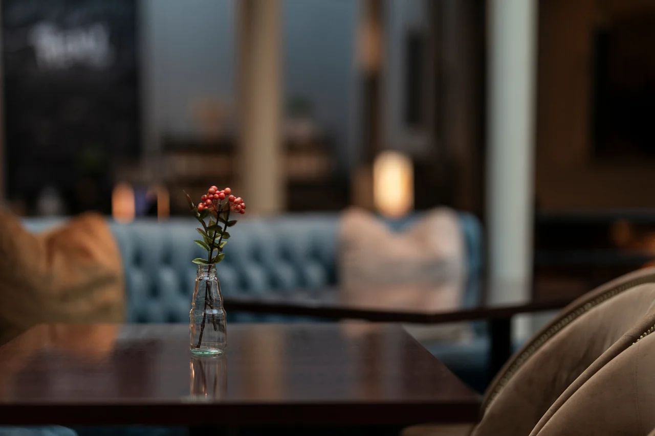 A cozy hotel lounge with a small vase of red berries on a dark wooden table. Home Hotel Grand Bodø.