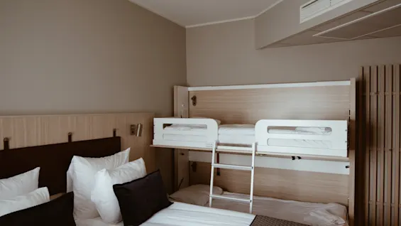 Et moderne og komfortabelt hotellrom med en stor seng og en innebygd køyeseng, designet for flere gjester.