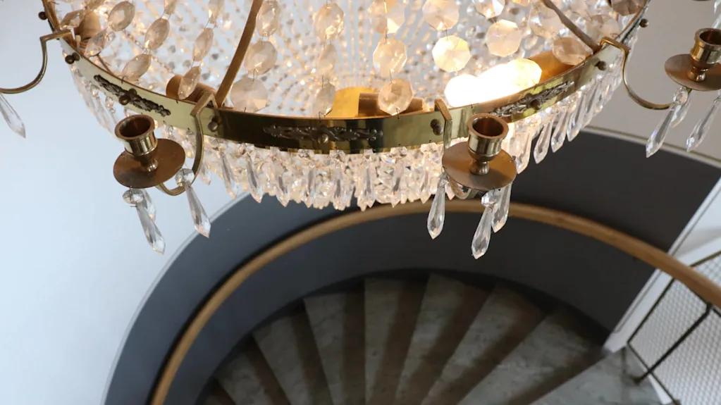A crystal chandelier hangs above a spiral staircase.
