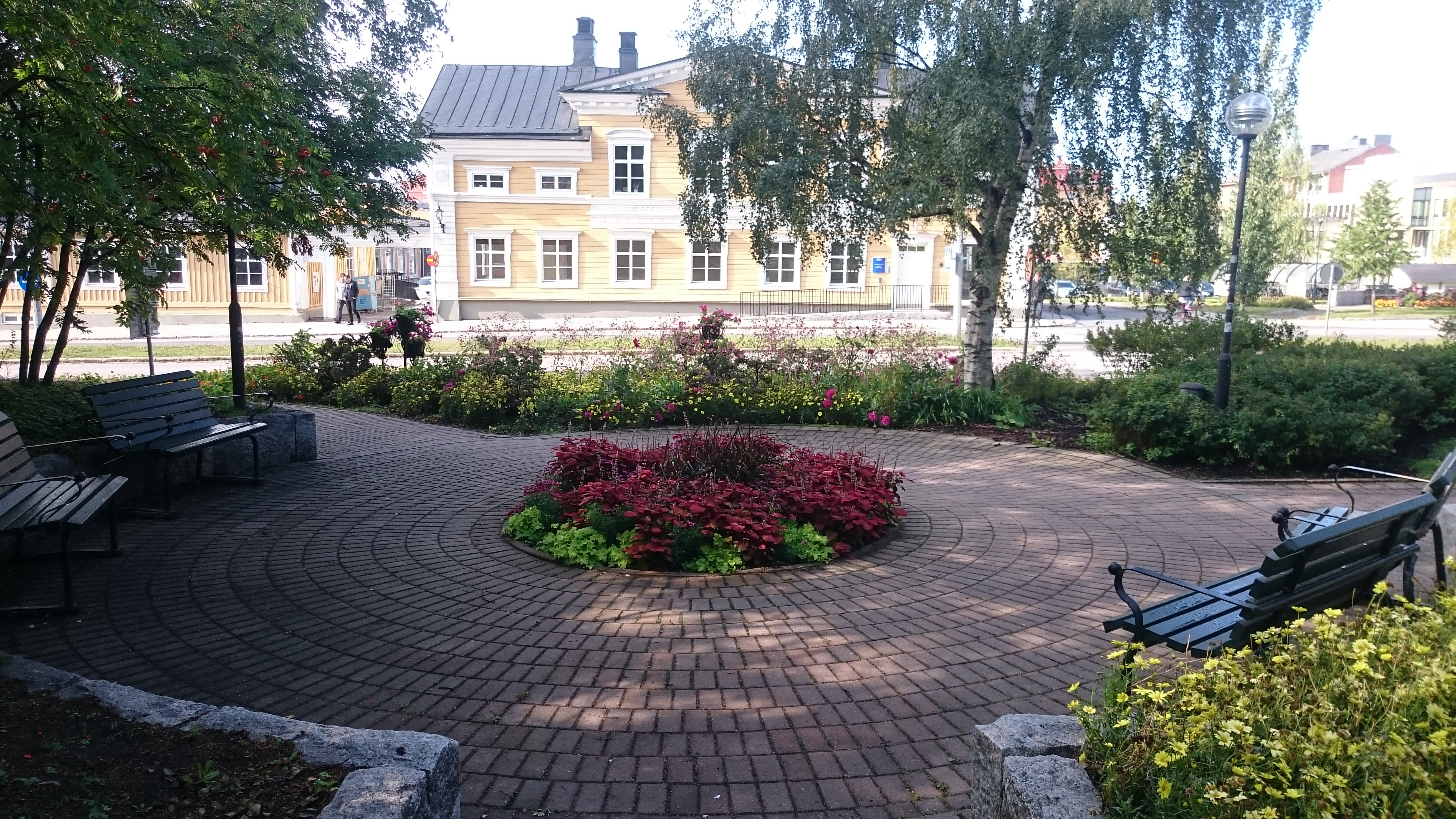 Red flower bed and benches outside yellow historic building in Lulea