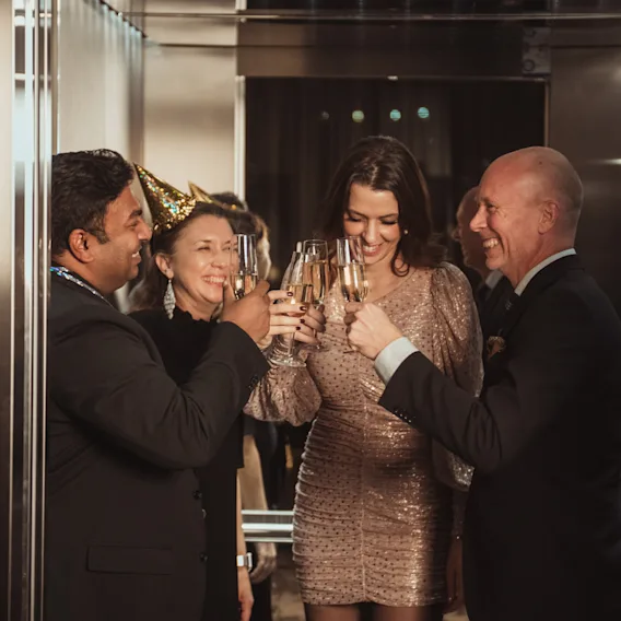 En gruppe glade mennesker skåler med champagneglass og feirer en spesiell anledning. En person har på seg en festhatt.