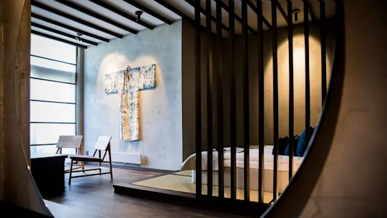 Et moderne soverom sett gjennom et ovalt speil, inneholder en kimono på veggen og trelemmer som skiller soveområdet.