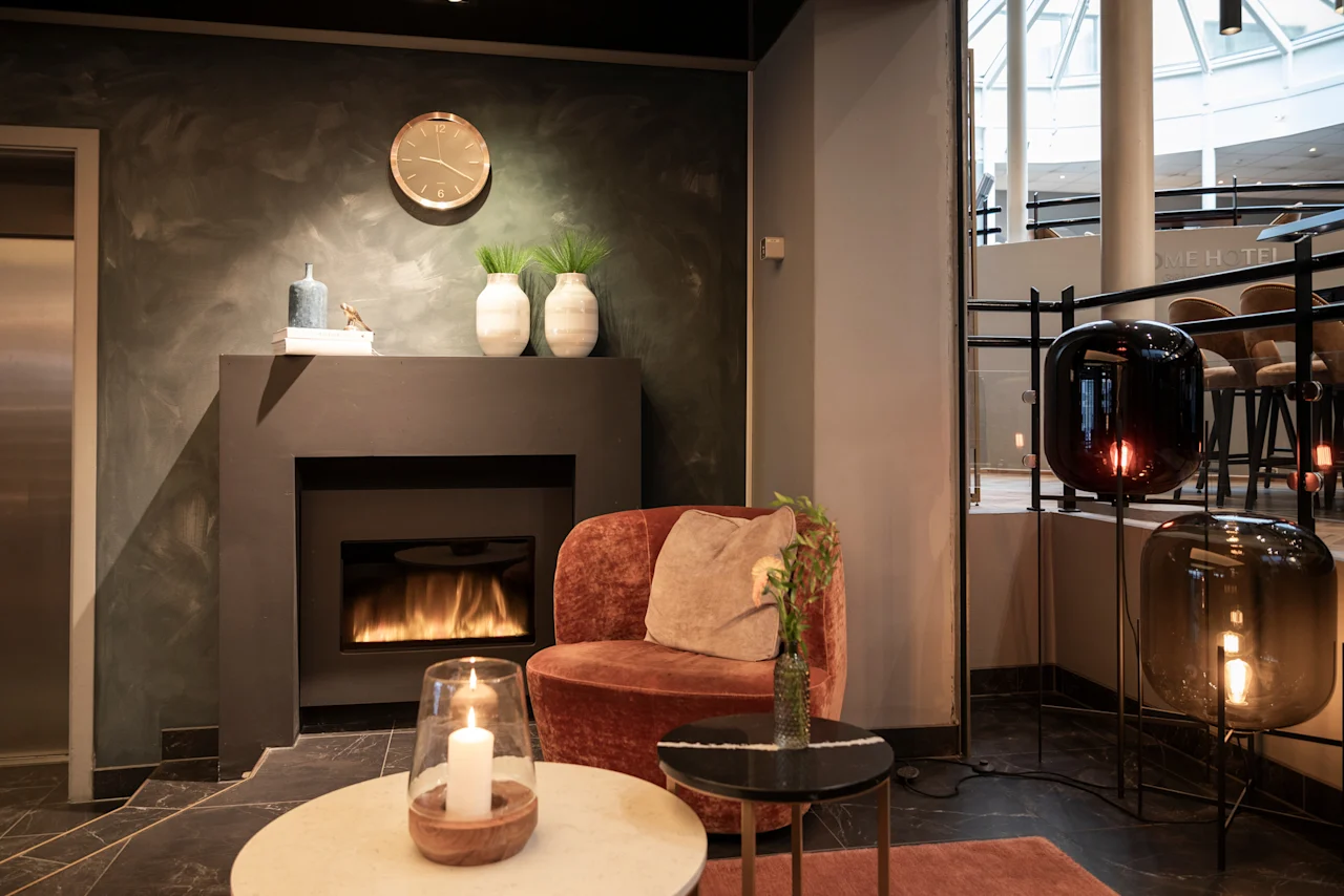 A warm and inviting hotel lounge with a lit fireplace and comfortable seating. Home Hotel Grand Bodø.