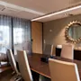 Et konferencetable omgivet af stole står i et mødelokale med et dekorativt solspejl på væggen, lette forhæng og blød belysning, der skaber en professionel atmosfære.