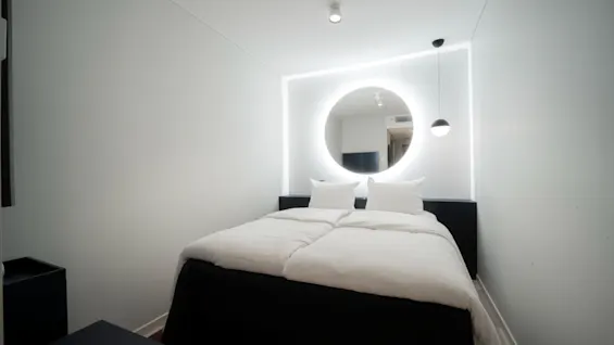 Et moderne og minimalistisk hotellrom på Quality Hotel Strawberry Arena, med en komfortabel seng og et bakgrunnsbelyst sirkulært speil.