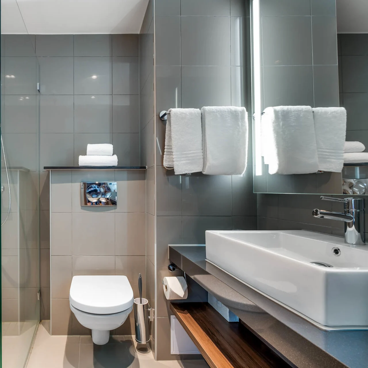A modern bathroom with a glass-enclosed shower, towel rack, toilet, and sink against tiled walls.
