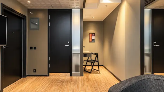 Modern hotel hallway with wooden floors, dark doors, and a small workstation with a chair.