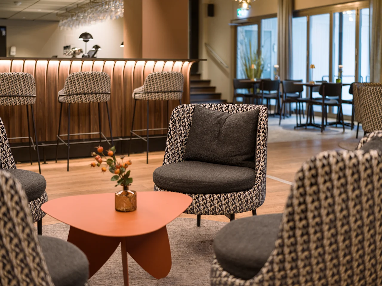 Bekväma stolar omger ett litet, modernt bord med en växt i en stilfull lounge med bar och höga pallar i bakgrunden.