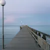 En lang trebrygge som strekker seg ut i det rolige havet i Falkenberg under en myk pastelthimmel.