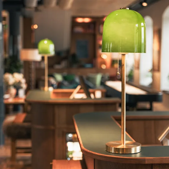 Cozy hotel reception desk with warm wooden counters and glowing green glass table lamps.