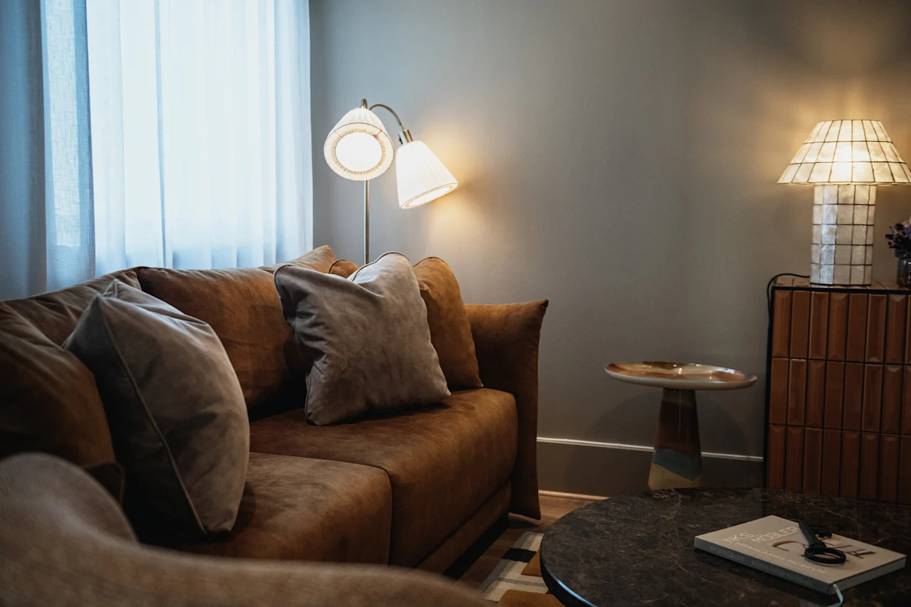 Ett varmt och inbjudande vardagsrum med en bekväm brun soffa med mjuka kuddar, upplyst av mjukt lampljus.
