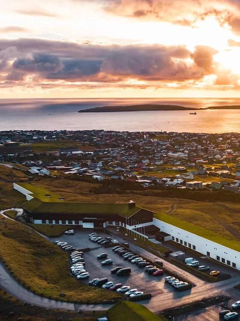 Luftfoto af en kystby ved solnedgang med bygninger, biler og havet.