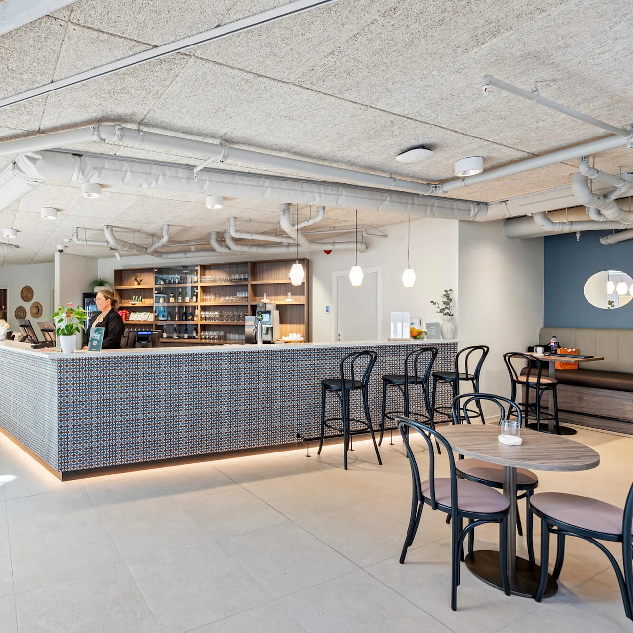 A reception area with a patterned front desk and a staff member, within a well-lit modern interior featuring seating and decorative elements.