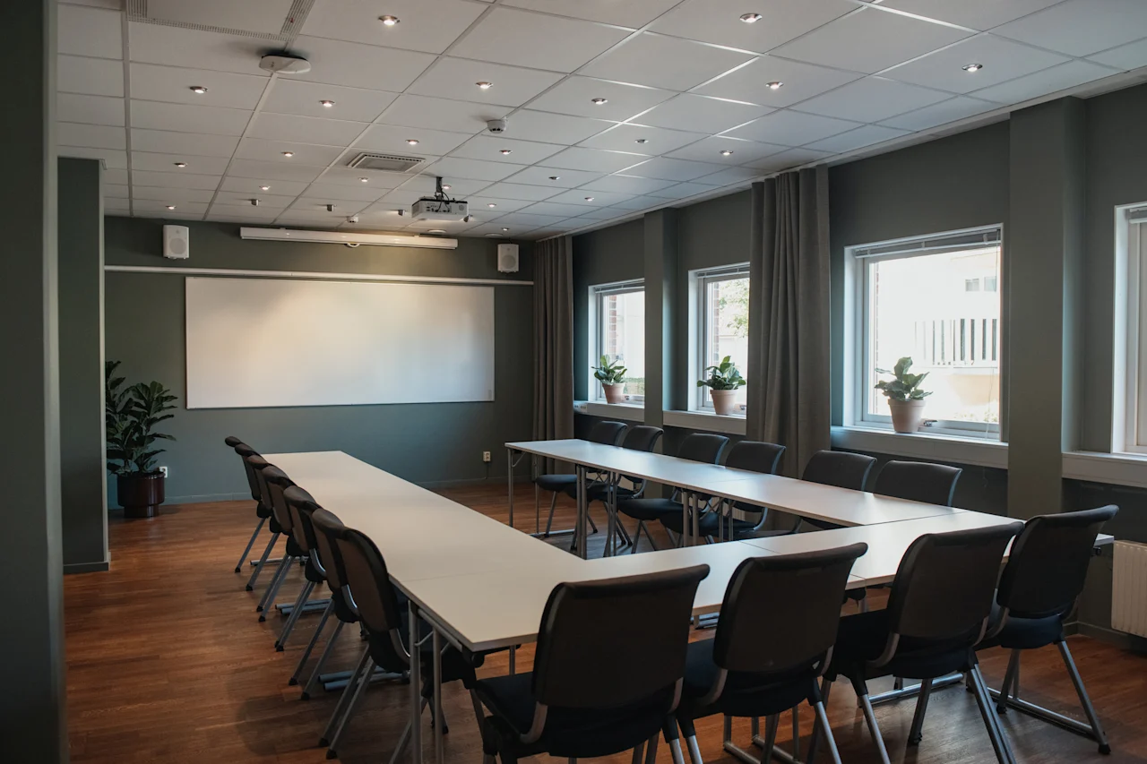 Ett modernt konferensrum med U-formad bordsuppställning, en stor whiteboard och en projektor, redo för ett möte.