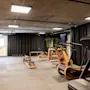 Løbebånd står stille i et moderne træningsstudie med træ-træningsudstyr, mørke gardiner og potteplanter, hvilket skaber et elegant, minimalistisk træningsrum.