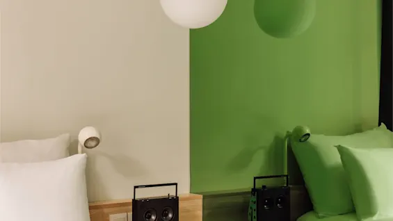 Hobo Oslo hotel room with modern design, two-toned wall, white and green beds, and speakers on nightstands.
