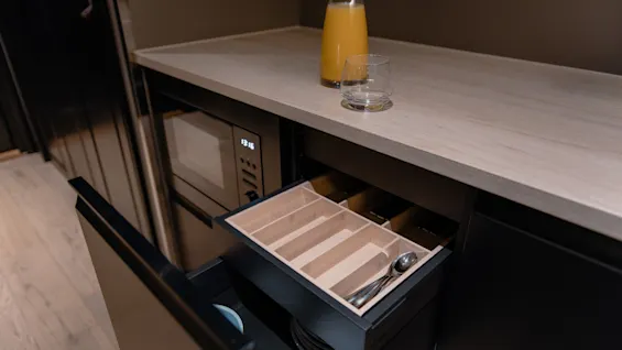Hotellrom med kjøkkenkrok, med mikrobølgeovn, juice og en åpen skuff med bestikk og servise.