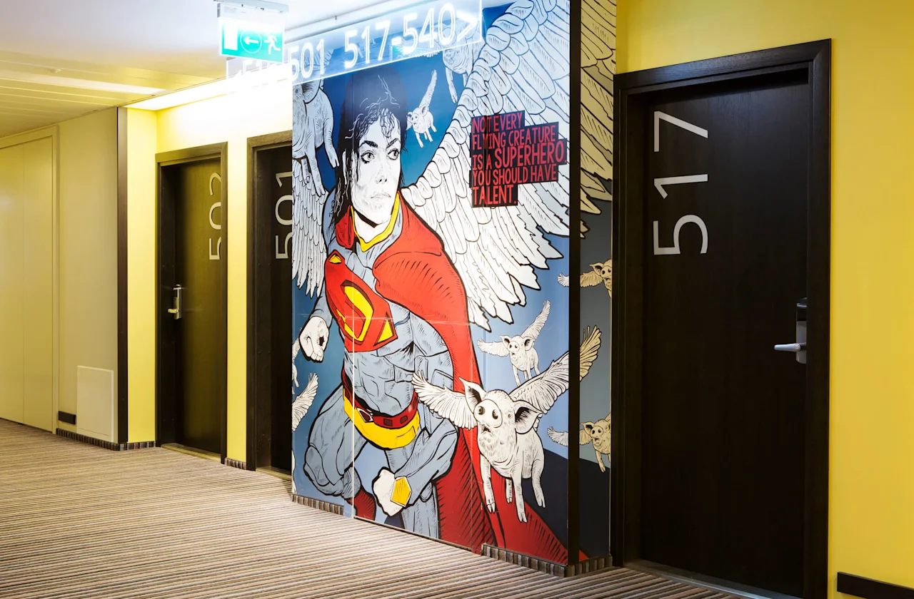 A mural depicts a caped superhero with wings, flanked by flying creatures, next to hotel room doors numbered 501 and 517. Text reads: "Not every flying creature is a superhero. You should have talent."