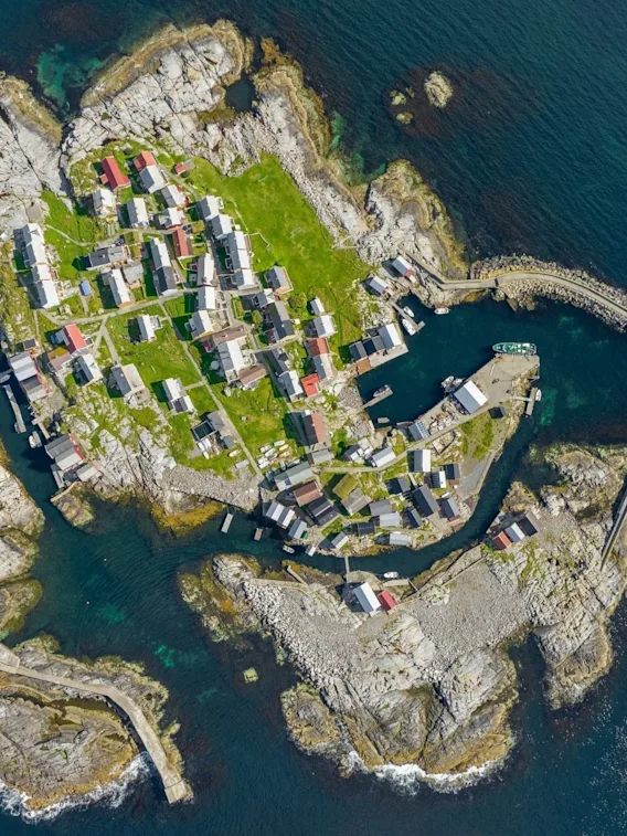 Luftfoto av en liten, steinete øy med tett bebyggelse og en lun havn omkranset av blått hav.